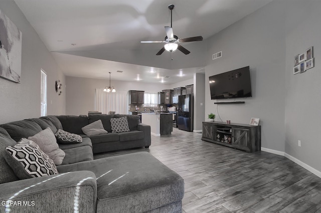 living room featuring lofted ceiling, dark wood-type flooring, and ceiling fan with notable chandelier