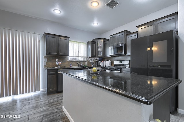 kitchen featuring a center island, stainless steel appliances, dark stone counters, decorative backsplash, and dark brown cabinets