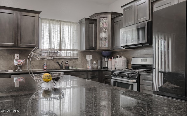 kitchen featuring dark brown cabinetry, sink, dark stone countertops, decorative backsplash, and appliances with stainless steel finishes