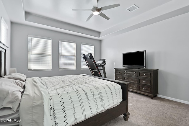 bedroom with multiple windows, light colored carpet, ceiling fan, and a tray ceiling