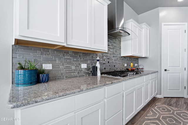 kitchen with light stone countertops, wall chimney exhaust hood, stainless steel gas cooktop, dark wood-type flooring, and white cabinets