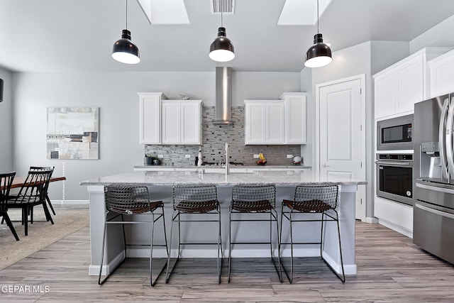 kitchen featuring white cabinets, wall chimney range hood, and appliances with stainless steel finishes