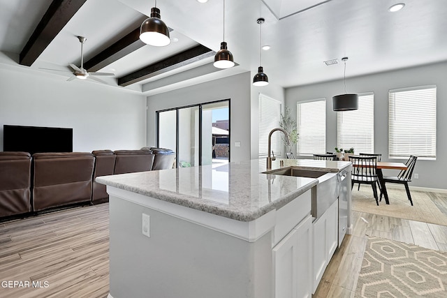 kitchen with light hardwood / wood-style flooring, an island with sink, decorative light fixtures, light stone counters, and white cabinetry