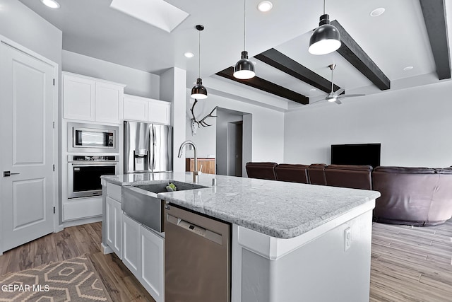 kitchen with beamed ceiling, white cabinetry, an island with sink, and appliances with stainless steel finishes