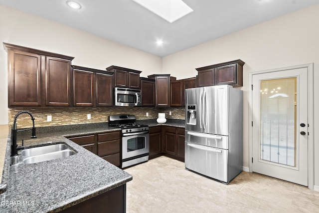 kitchen featuring appliances with stainless steel finishes, a skylight, sink, dark stone counters, and decorative backsplash