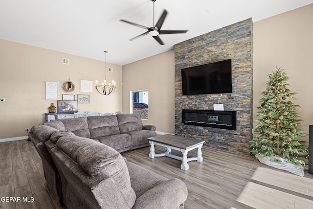 living room featuring hardwood / wood-style floors, ceiling fan with notable chandelier, and a stone fireplace