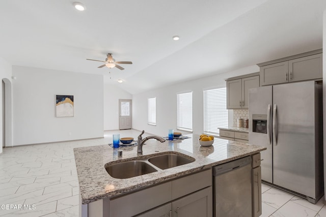 kitchen with light stone countertops, stainless steel appliances, vaulted ceiling, sink, and an island with sink