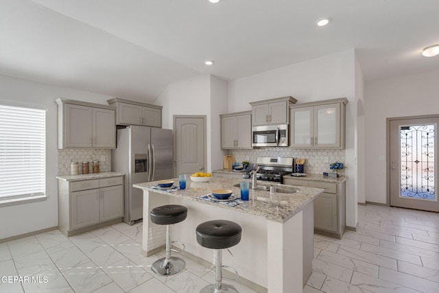 kitchen with sink, backsplash, a breakfast bar, a center island with sink, and appliances with stainless steel finishes