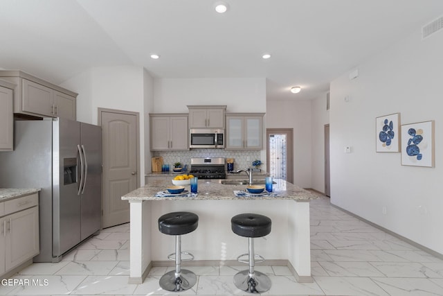 kitchen featuring light stone countertops, appliances with stainless steel finishes, a breakfast bar, sink, and an island with sink