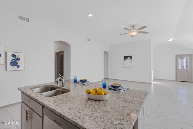 kitchen featuring lofted ceiling, a kitchen island with sink, sink, stainless steel dishwasher, and light stone counters