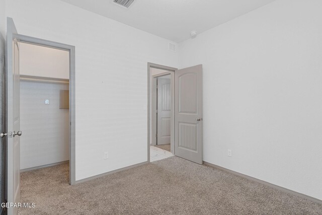 unfurnished bedroom with a walk in closet, a closet, and light colored carpet