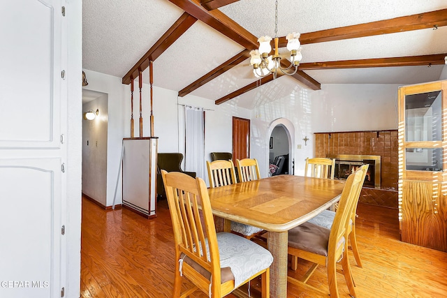 dining space with a tile fireplace, lofted ceiling with beams, a notable chandelier, hardwood / wood-style floors, and a textured ceiling