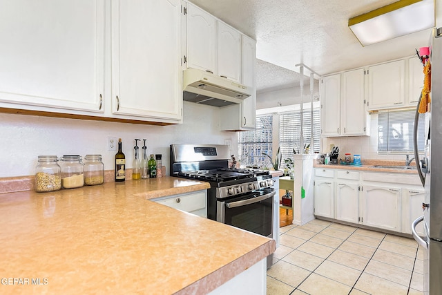 kitchen with a textured ceiling, gas stove, sink, light tile patterned floors, and white cabinetry