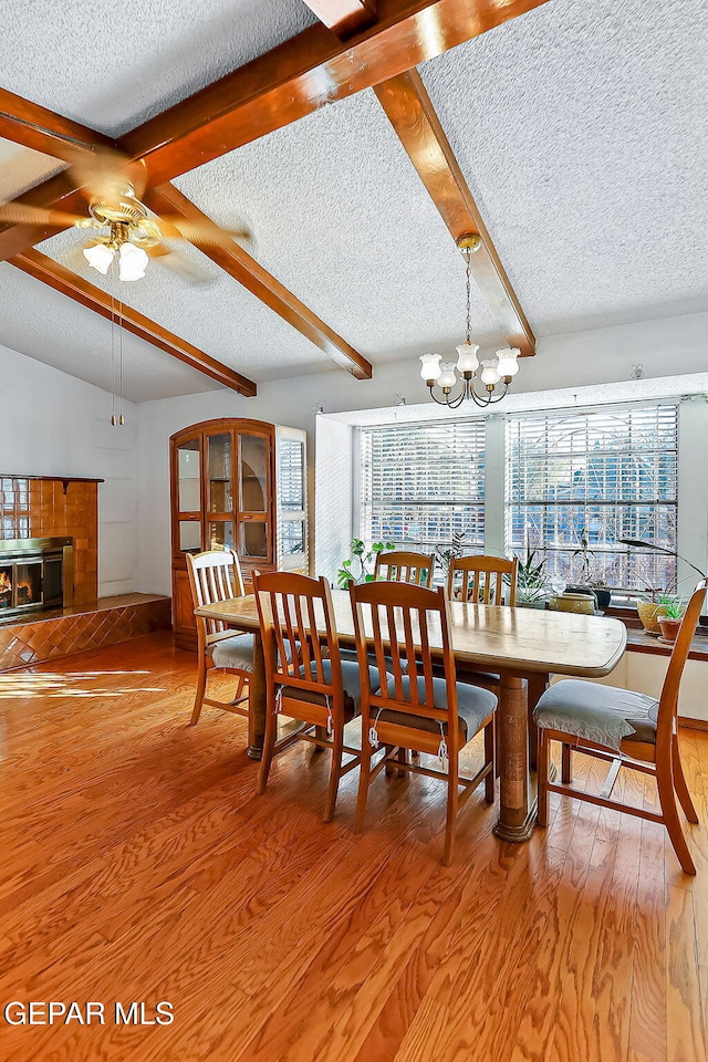 dining area with ceiling fan with notable chandelier, hardwood / wood-style floors, a textured ceiling, and a tiled fireplace