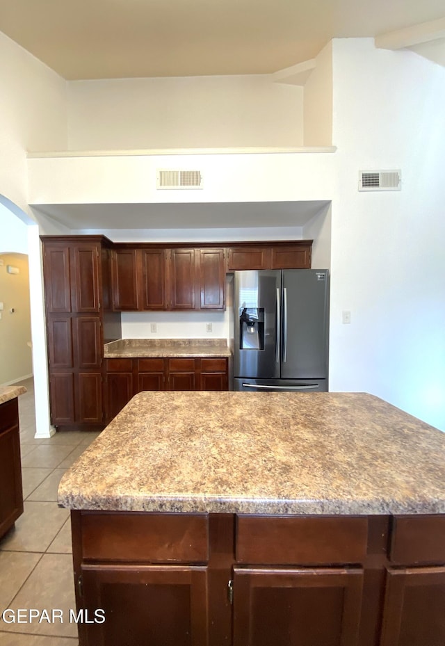 kitchen with a center island, dark brown cabinets, stainless steel fridge, and light tile patterned flooring