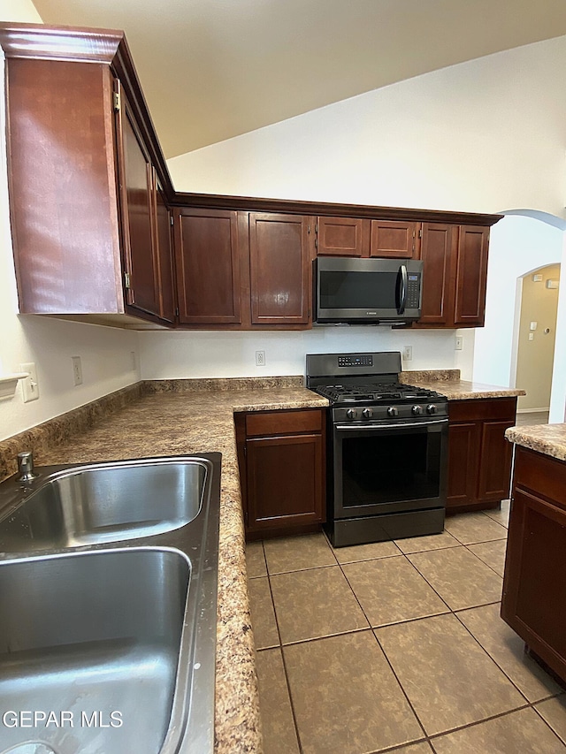 kitchen with lofted ceiling, black gas stove, sink, light tile patterned floors, and dark brown cabinets