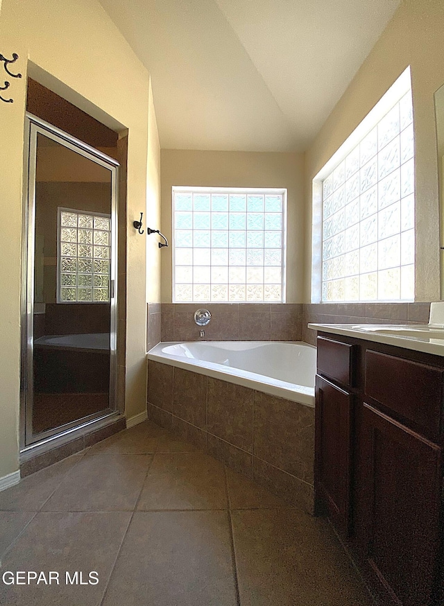 bathroom featuring vanity, tile patterned floors, lofted ceiling, and tiled tub