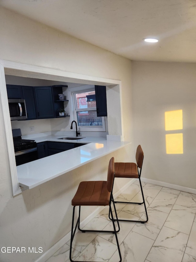 kitchen with black range with gas stovetop, sink, blue cabinetry, kitchen peninsula, and a breakfast bar area