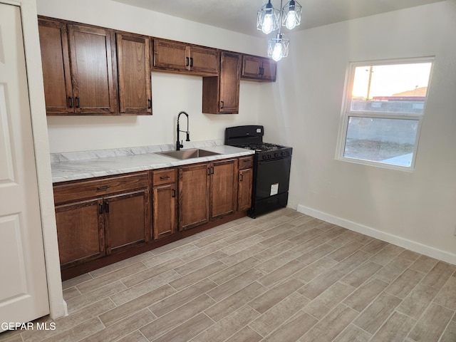 kitchen with decorative light fixtures, gas stove, light wood-type flooring, and sink