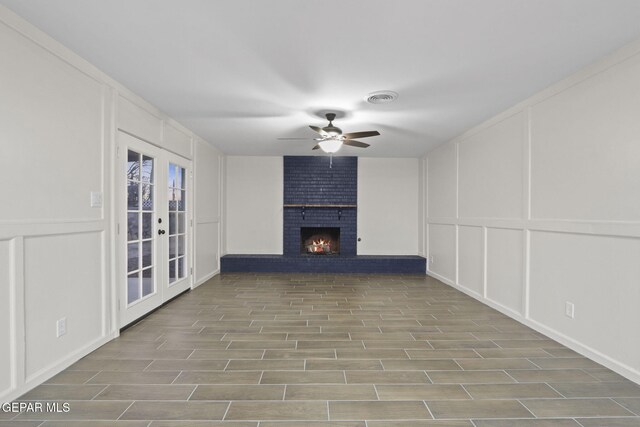 unfurnished living room featuring a brick fireplace, ceiling fan, french doors, and light wood-type flooring