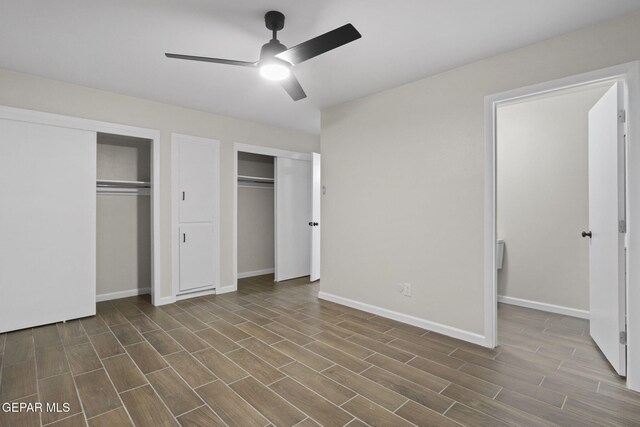 unfurnished bedroom featuring multiple closets, ceiling fan, and wood-type flooring