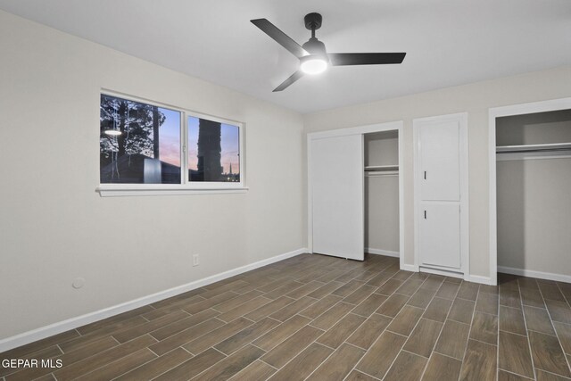 unfurnished bedroom with dark hardwood / wood-style floors, ceiling fan, and multiple closets