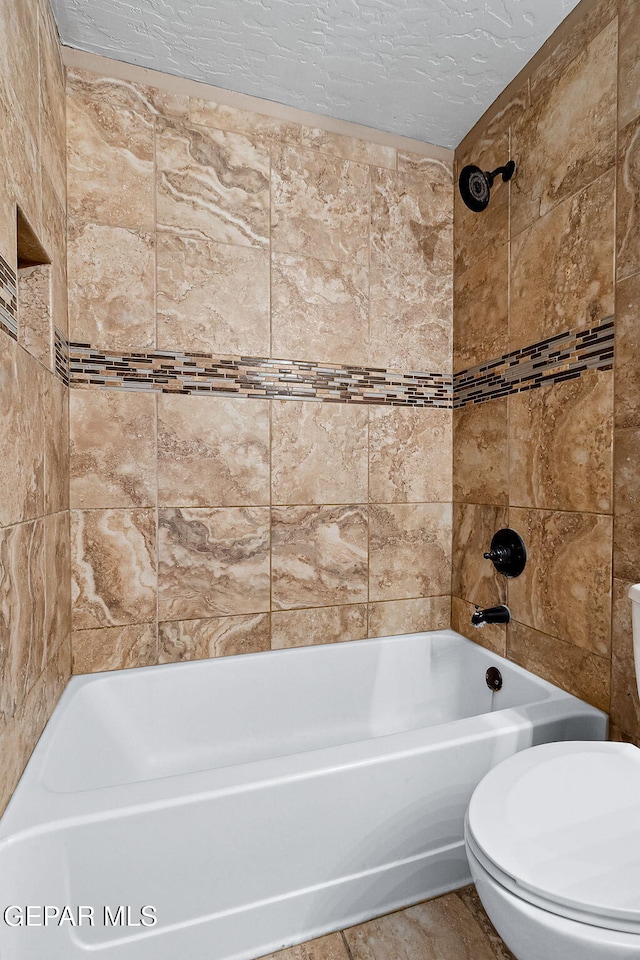 bathroom with a textured ceiling, toilet, and tiled shower / bath