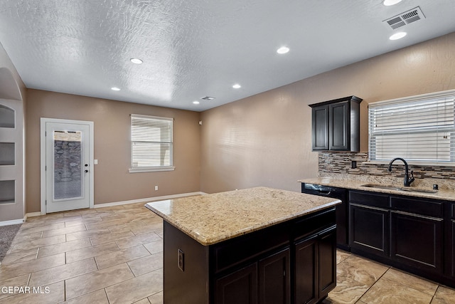 kitchen featuring decorative backsplash, a center island, light stone countertops, and sink