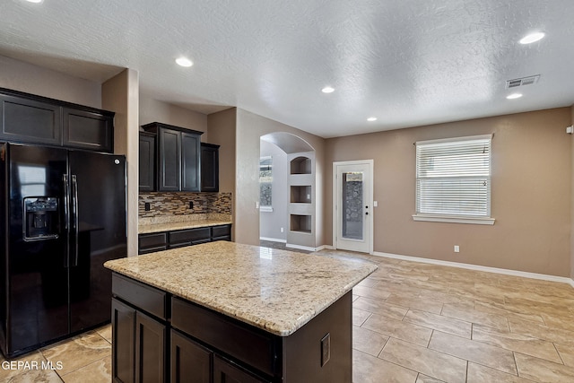 kitchen featuring light stone countertops, a center island, backsplash, a textured ceiling, and black fridge with ice dispenser