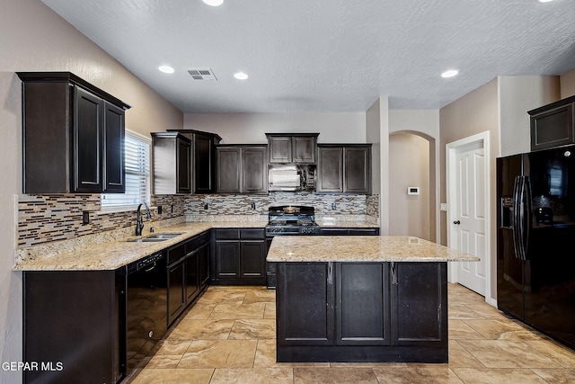 kitchen featuring tasteful backsplash, light stone counters, sink, black appliances, and a kitchen island