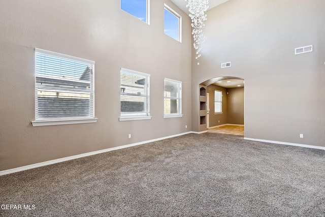 unfurnished living room with carpet, a towering ceiling, and a notable chandelier