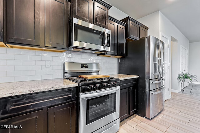 kitchen featuring appliances with stainless steel finishes, tasteful backsplash, dark brown cabinets, light hardwood / wood-style floors, and light stone counters