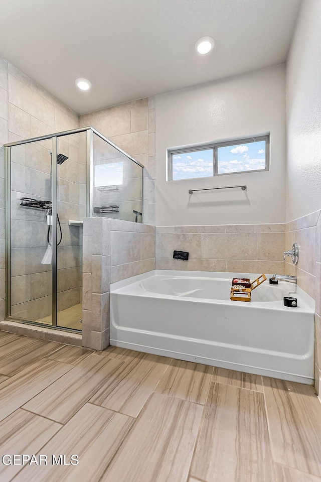 bathroom featuring shower with separate bathtub and tile walls