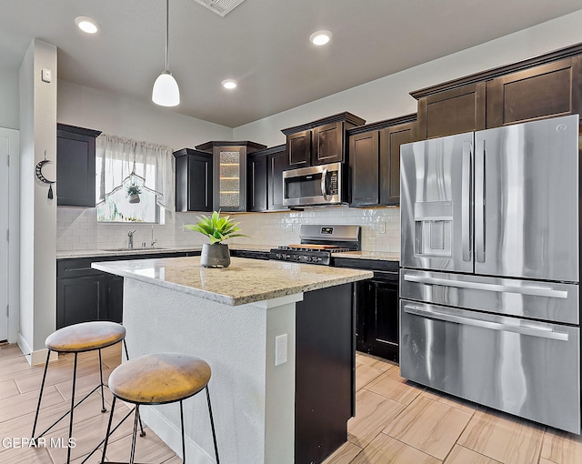 kitchen with light stone countertops, sink, stainless steel appliances, pendant lighting, and a kitchen island