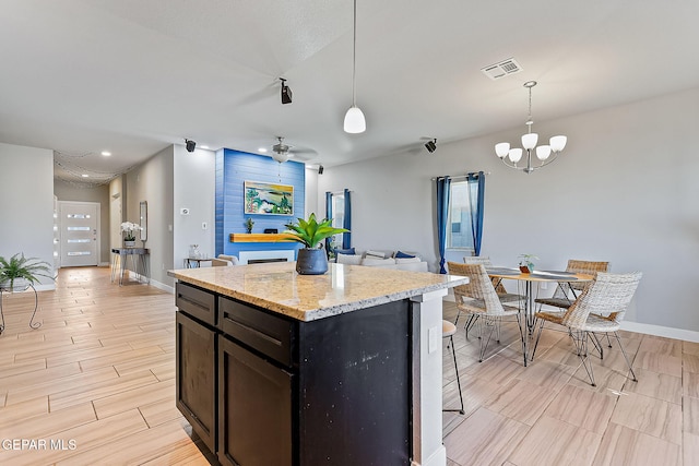 kitchen featuring light stone countertops, ceiling fan with notable chandelier, a kitchen island, and hanging light fixtures