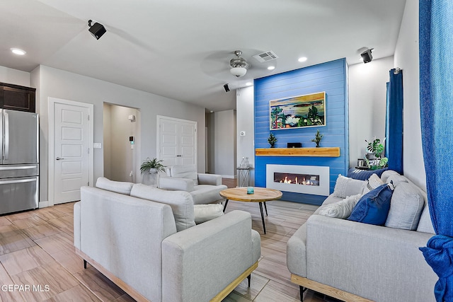 living room featuring ceiling fan, a large fireplace, and light wood-type flooring