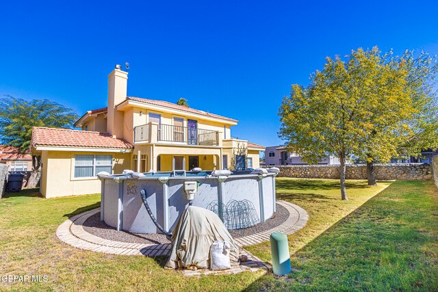 back of property featuring a balcony, a yard, and a covered pool