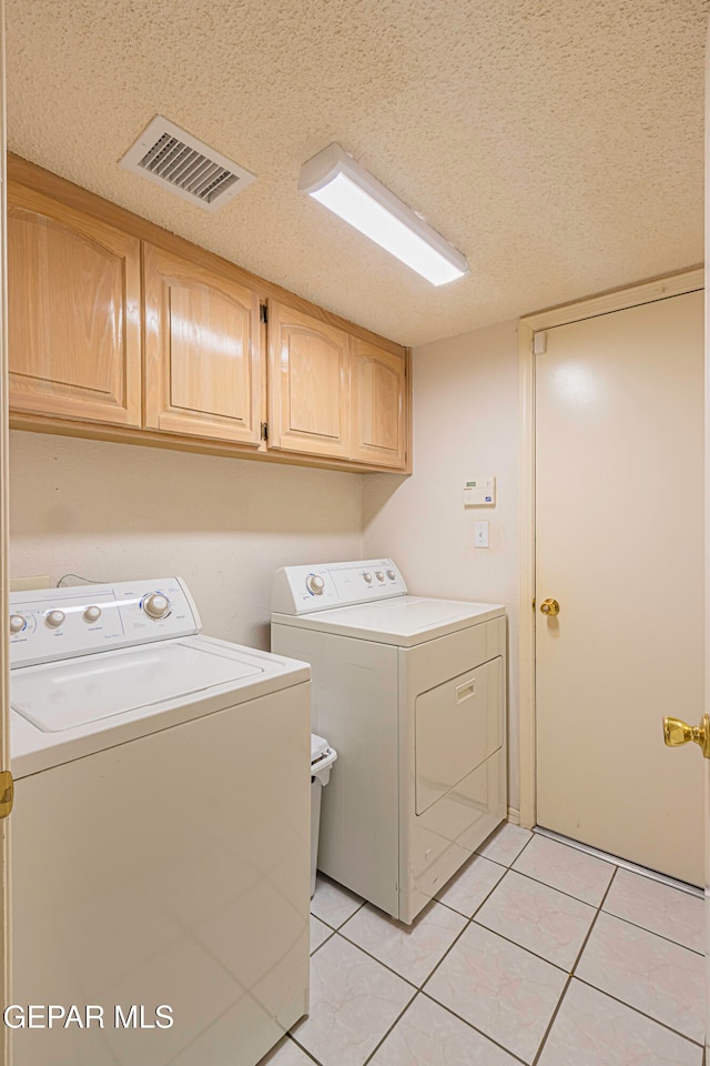 laundry room with washing machine and dryer, light tile patterned floors, cabinets, and a textured ceiling