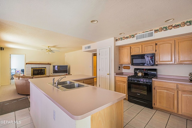 kitchen with a kitchen island with sink, a tile fireplace, black appliances, sink, and light tile patterned floors