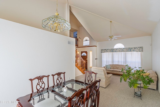 carpeted dining space with ceiling fan with notable chandelier and high vaulted ceiling