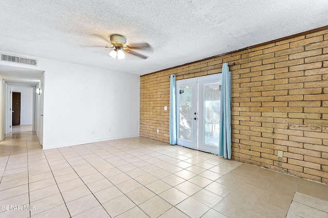 tiled empty room with french doors, a textured ceiling, ceiling fan, and brick wall