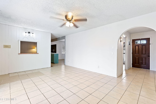 interior space featuring ceiling fan, wooden walls, light tile patterned flooring, and a textured ceiling