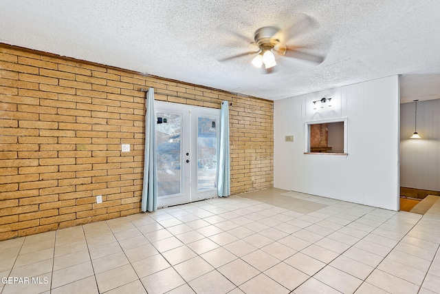 tiled empty room with ceiling fan, french doors, brick wall, and a textured ceiling