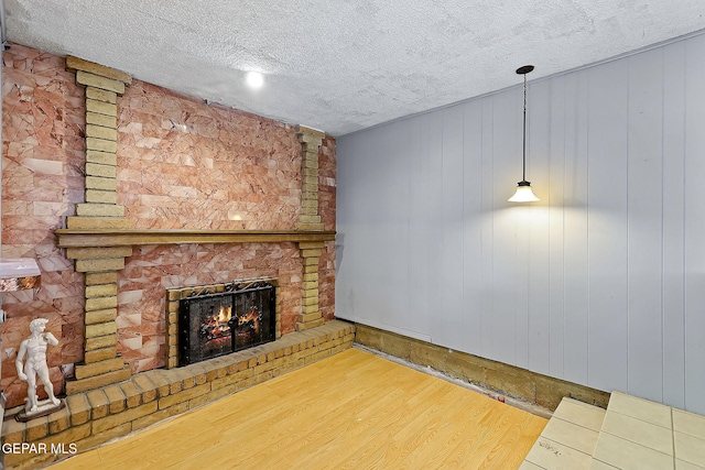 unfurnished living room with hardwood / wood-style floors, wood walls, a textured ceiling, and a brick fireplace