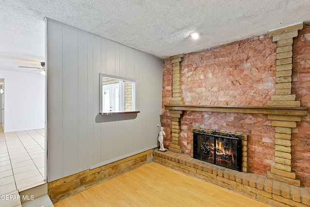 unfurnished living room featuring ceiling fan, a brick fireplace, wood walls, hardwood / wood-style floors, and a textured ceiling