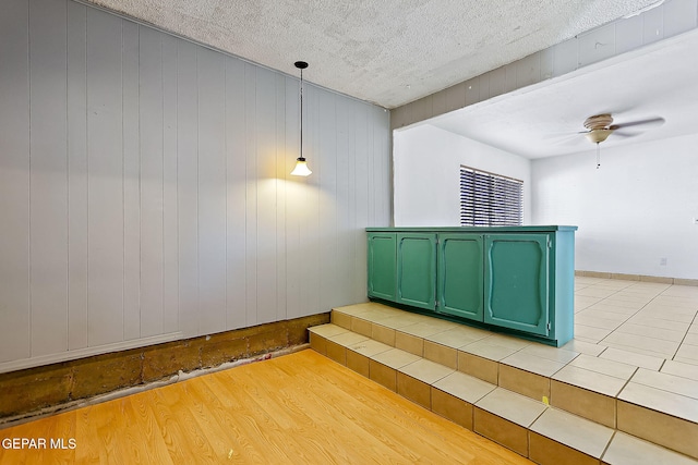 interior space featuring ceiling fan, wood walls, wood-type flooring, and a textured ceiling