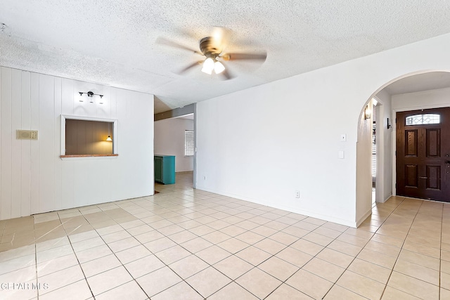 tiled empty room featuring a textured ceiling, ceiling fan, and wood walls