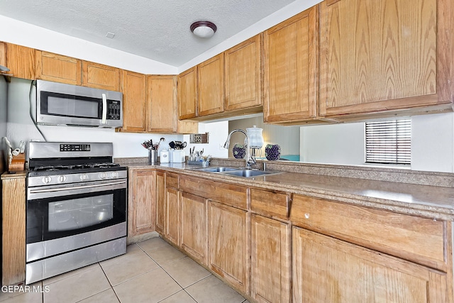 kitchen featuring sink, light tile patterned flooring, a textured ceiling, and appliances with stainless steel finishes