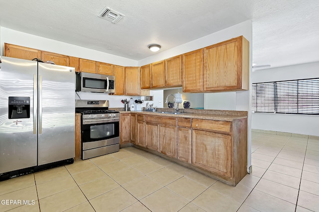 kitchen with a textured ceiling, light tile patterned floors, sink, and appliances with stainless steel finishes