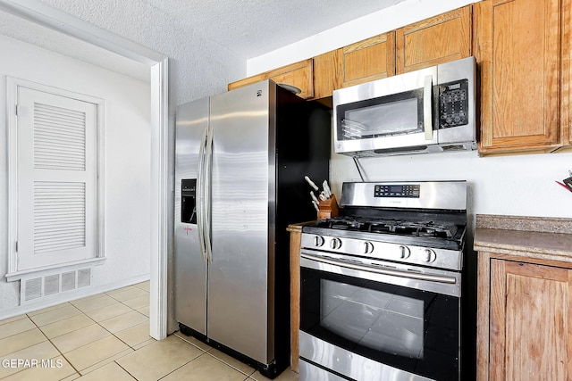 kitchen featuring light tile patterned flooring, a textured ceiling, and appliances with stainless steel finishes